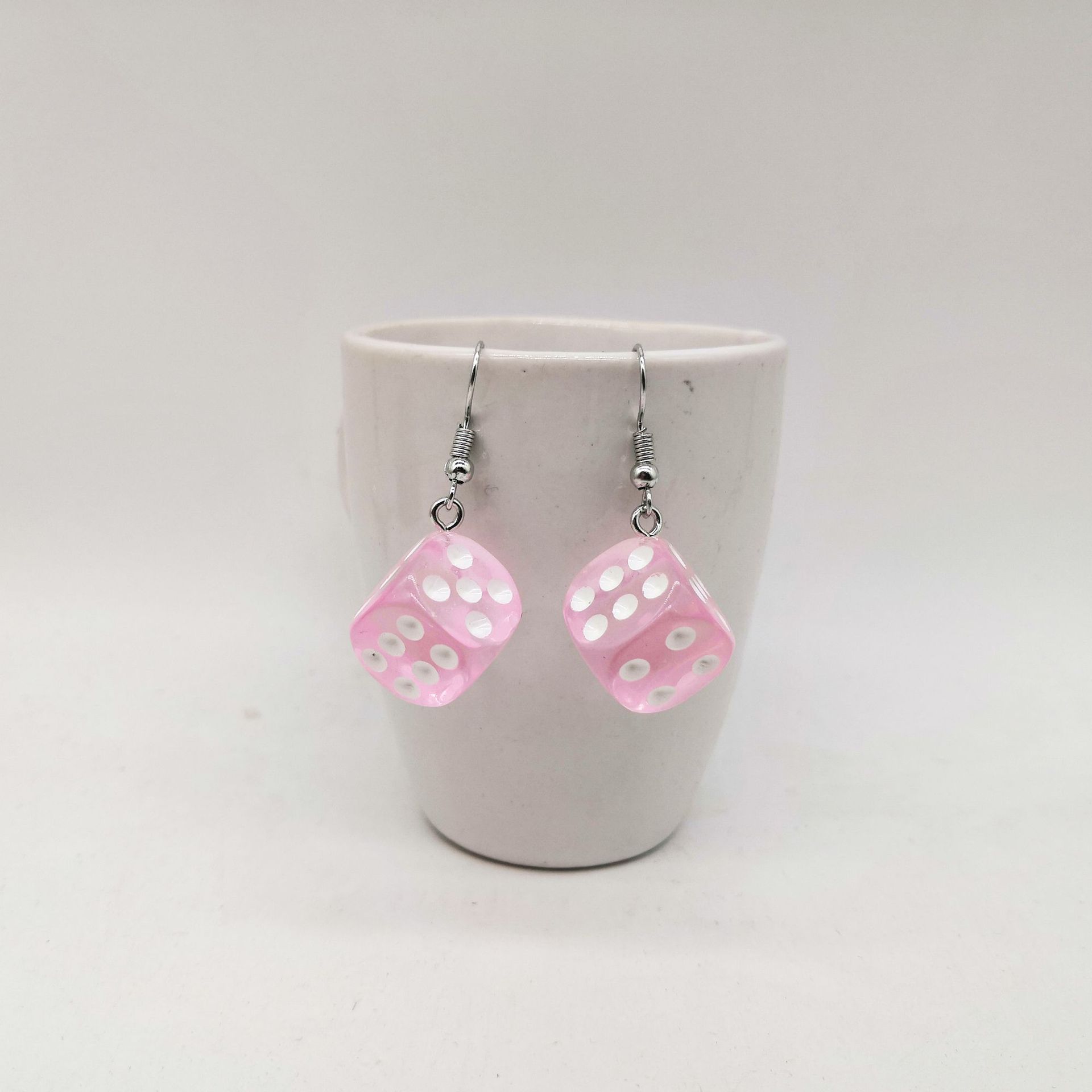 Rosa halvtransparenta retro tärningsörhängen i resin med vita prickar inspirerade av 1950-talets pinup- och rockabillykultur.